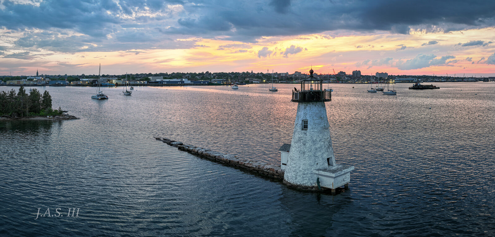 Palmer Island Light, a white lighthouse at the end of a stone breakwater, under a cloudy sky over New Bedford Harbor