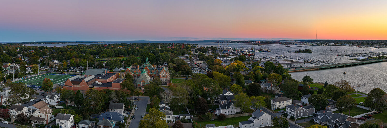 Rooftops and tree-lined streets of Fairhaven running toward the harbor at sunset, seen from above