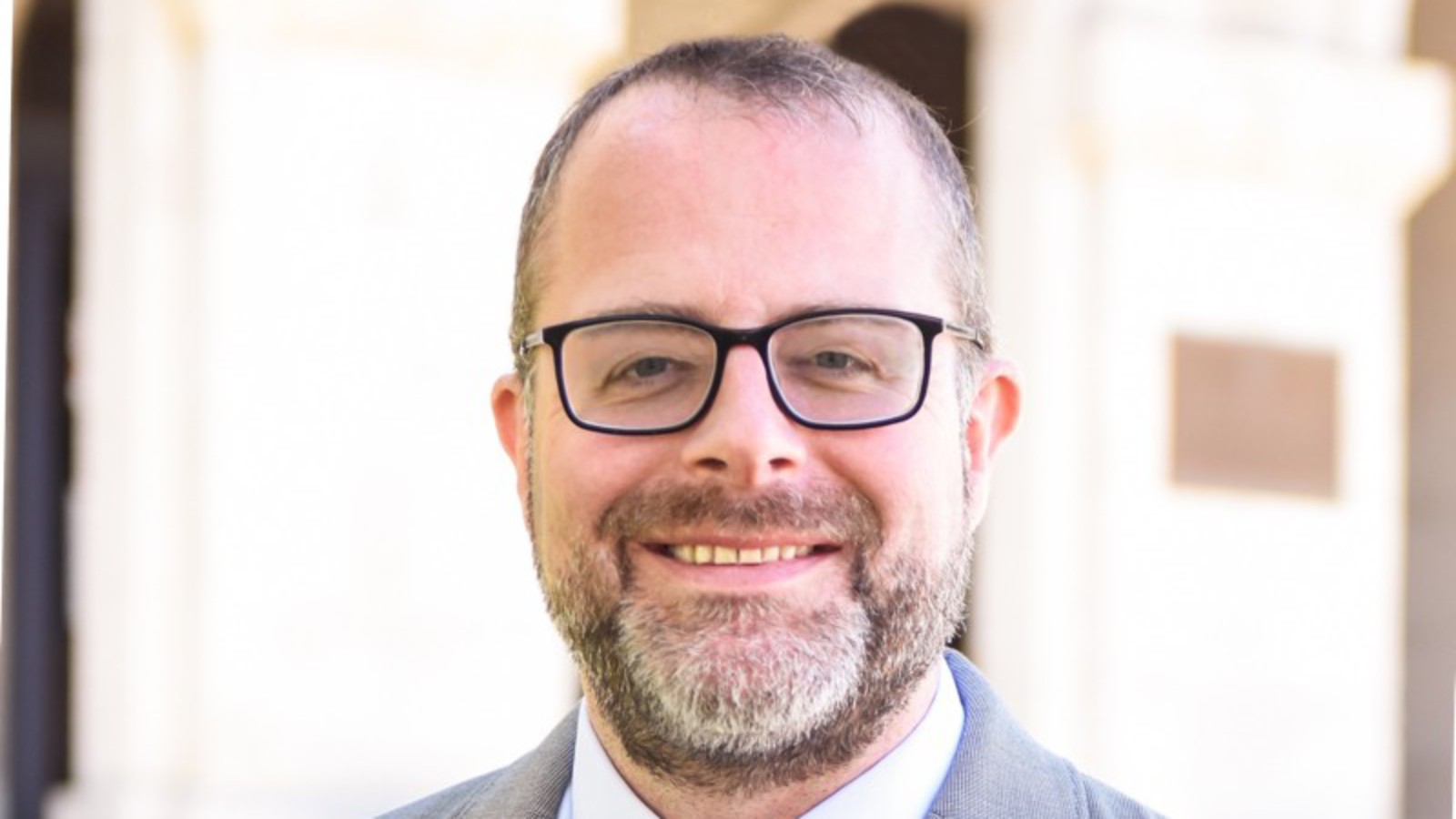 New Bedford Superintendent Andrew O'Leary, smiling, in glasses, a gray jacket and a blue striped tie
