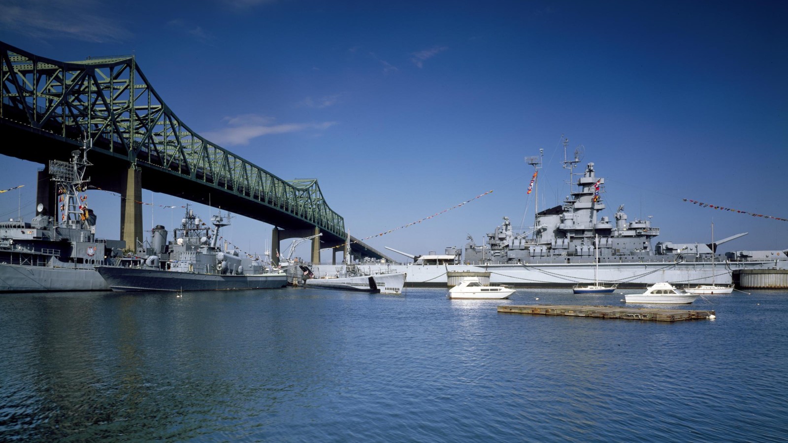 Battleship Cove in Fall River: the battleship USS Massachusetts and the destroyer USS Joseph P. Kennedy Jr. moored under the green steel Braga Bridge, with small boats on the water