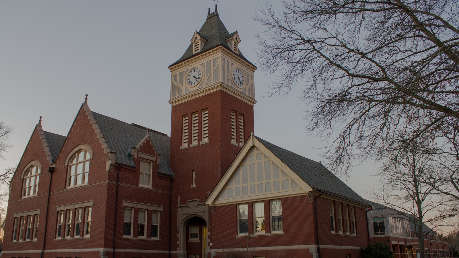Center School in Mattapoisett, a red brick school with a clock tower and cream trim, seen from the lawn at dusk with bare trees at right