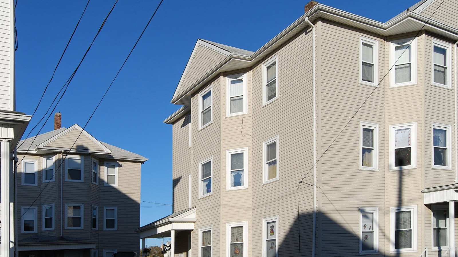 Three-story, three-family houses with tan siding and stacked windows along Albion Street in Fall River under a blue sky