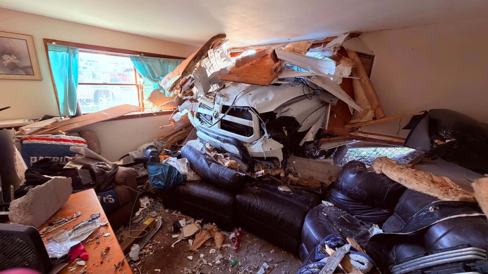 The crushed front of a white pickup truck pushed through the wall of a Fall River living room, with broken wood, insulation and a damaged leather couch around it