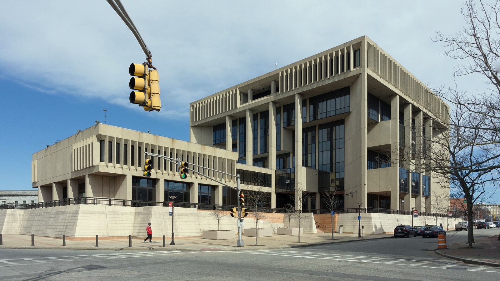 Fall River Government Center, the city's concrete City Hall, rising above a corner crosswalk with a traffic signal hanging in the foreground under a partly cloudy sky