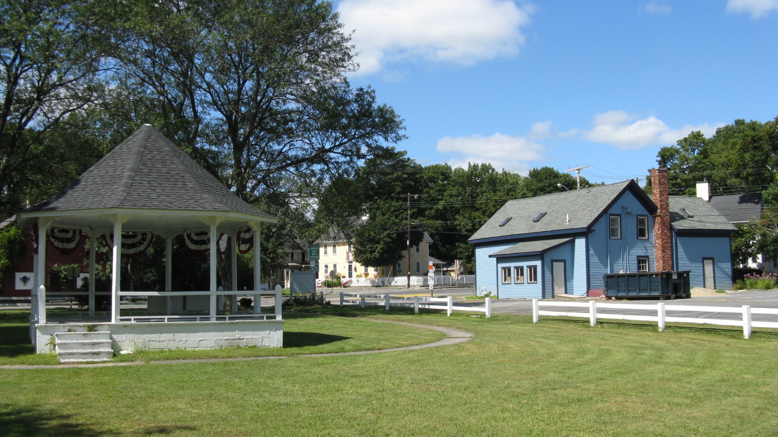 The gazebo on the Freetown Common in Assonet, with a blue house and white fence behind it