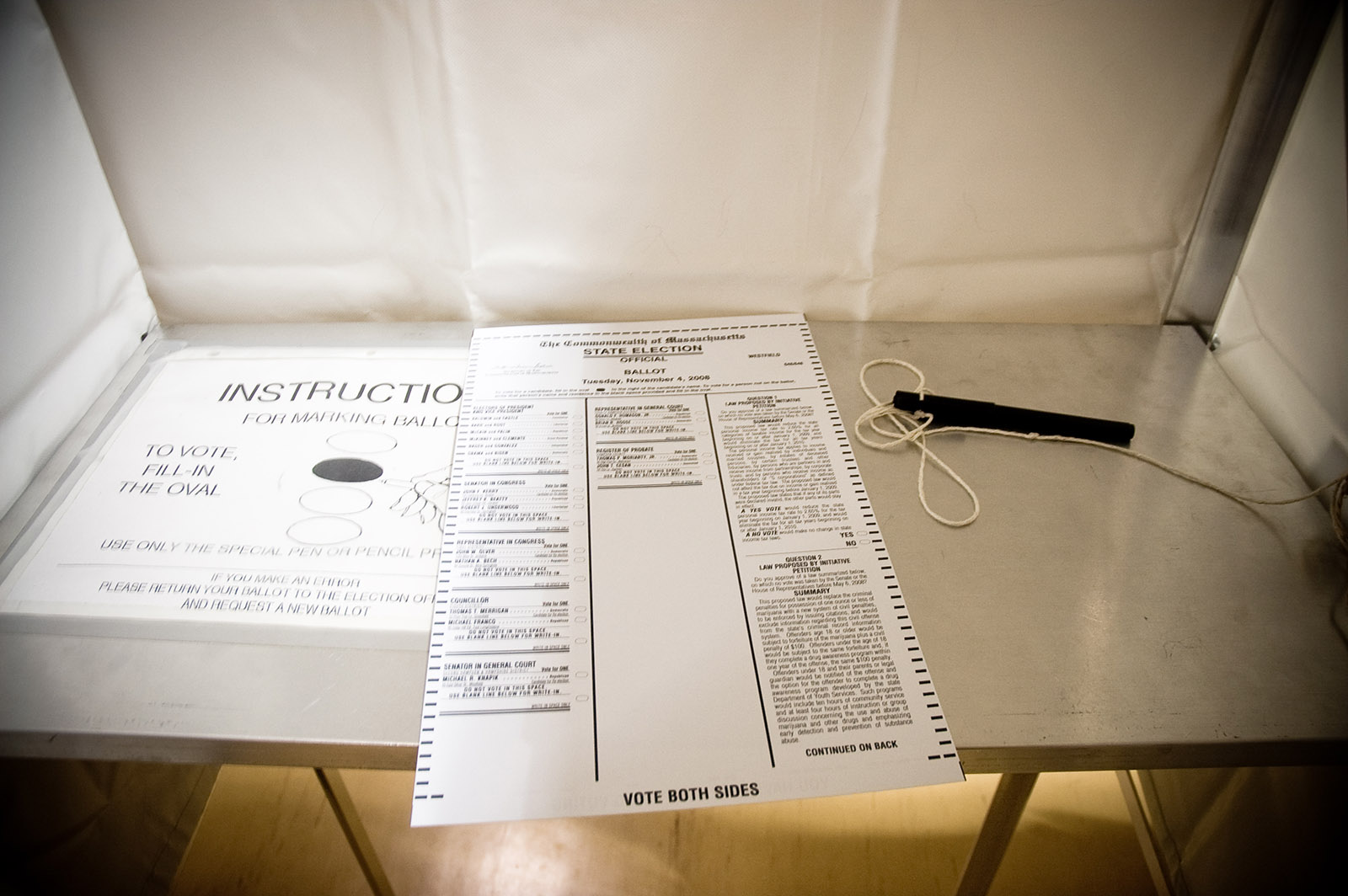 An official Massachusetts state election ballot on a voting booth shelf on Election Day, with the statewide ballot questions printed in the right-hand column