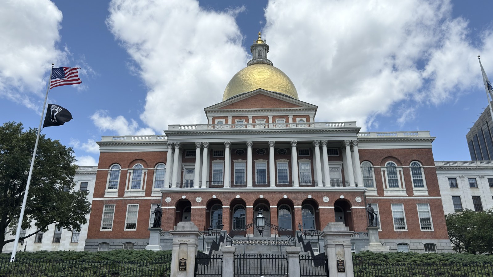 The Massachusetts State House on Beacon Street in Boston, its gold dome and brick front under a cloudy blue sky