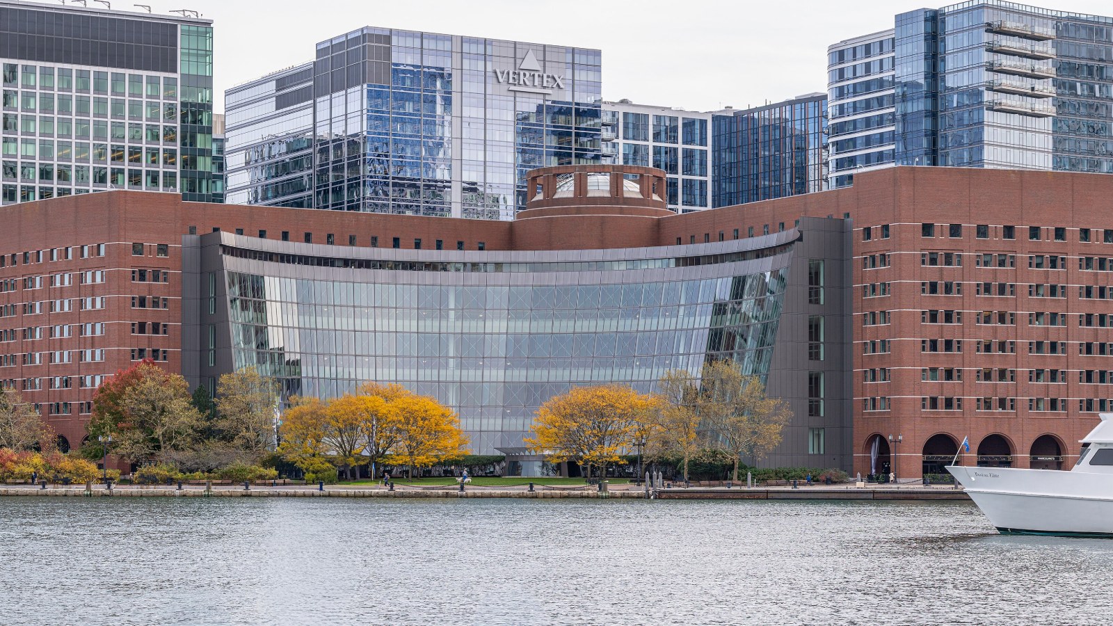 The brick and curved glass John Joseph Moakley United States Courthouse on the Boston waterfront, with yellow autumn trees along the harbor