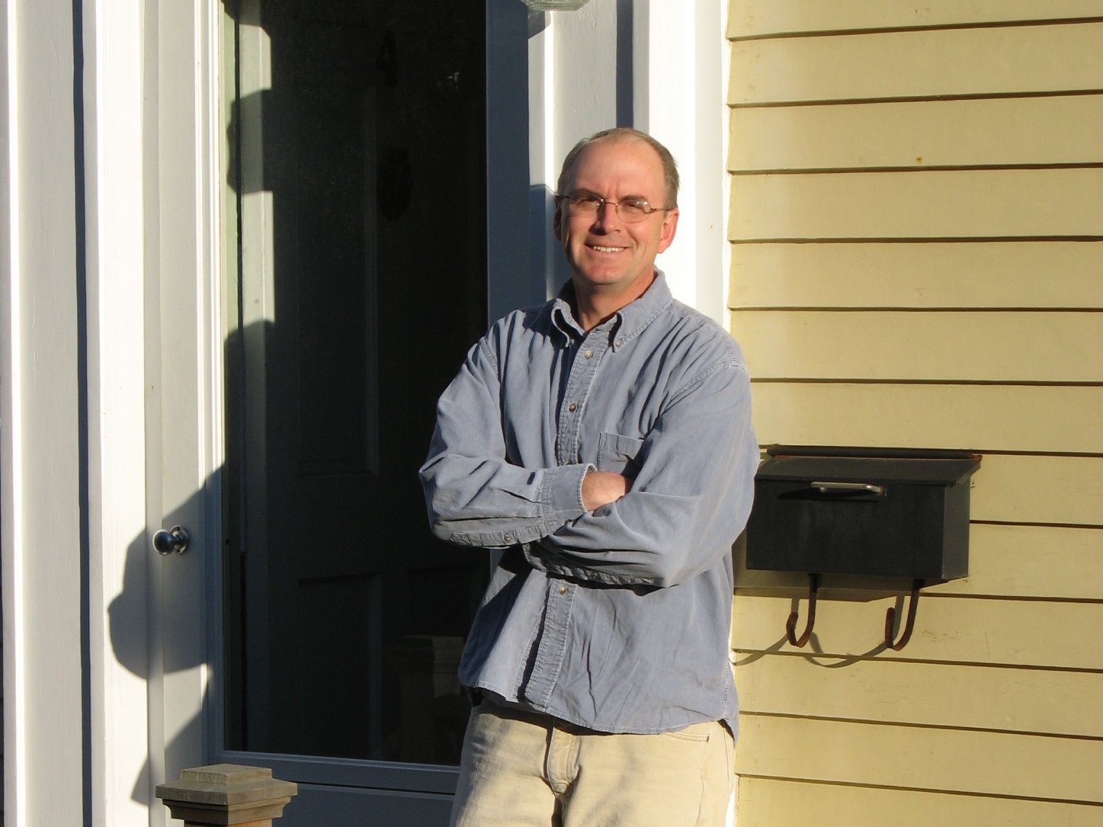 Author Nathaniel Philbrick, in a blue shirt, standing on the porch of a yellow clapboard house