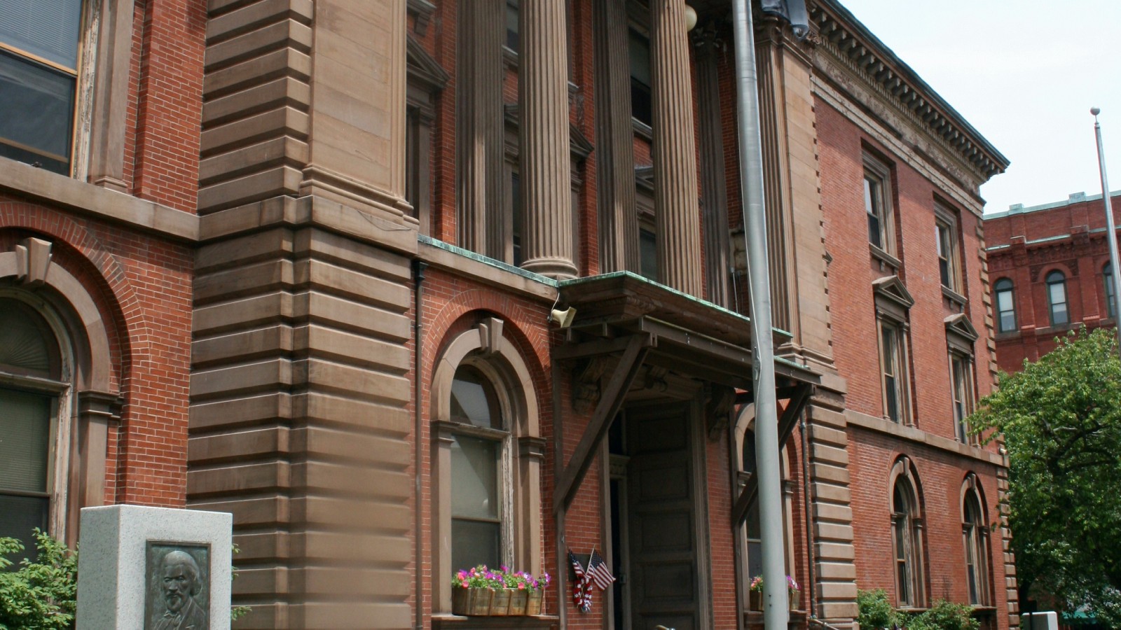 The front of New Bedford City Hall on William Street, with its tall stone columns over the entrance canopy, the front door and the flagpole