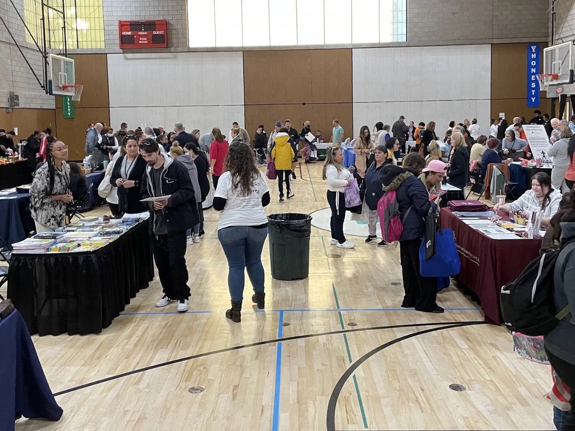 Visitors walk between service agency tables in a YMCA gym
