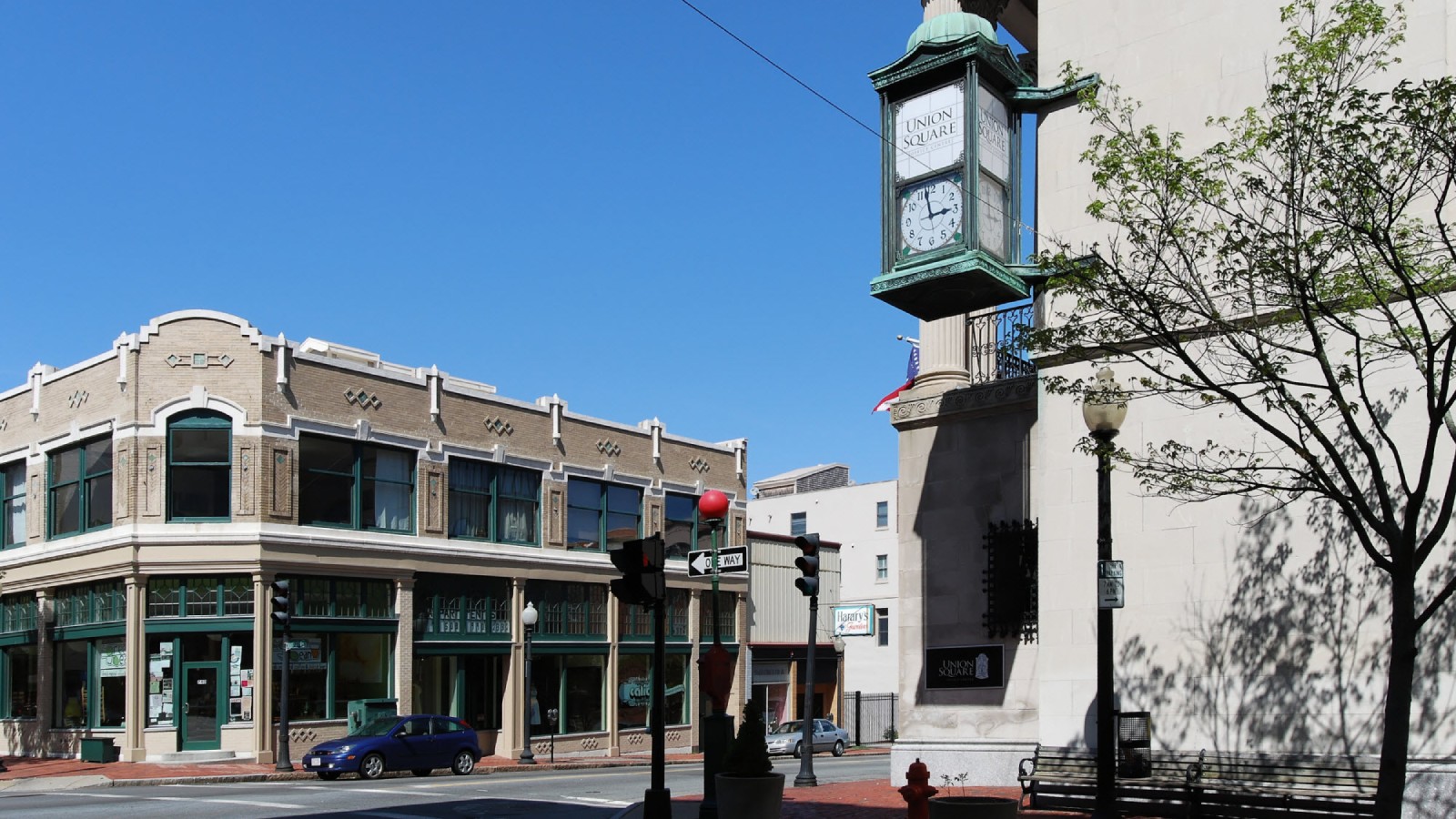 The Union Square clock on a granite corner building in downtown New Bedford, across the street from a two story tan brick block with green trimmed storefronts