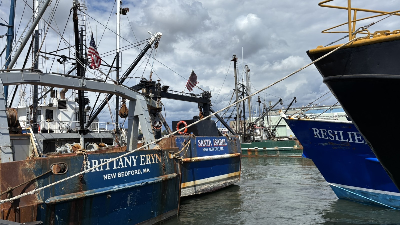 Fishing boats tied up at a pier in the Port of New Bedford under a cloudy sky