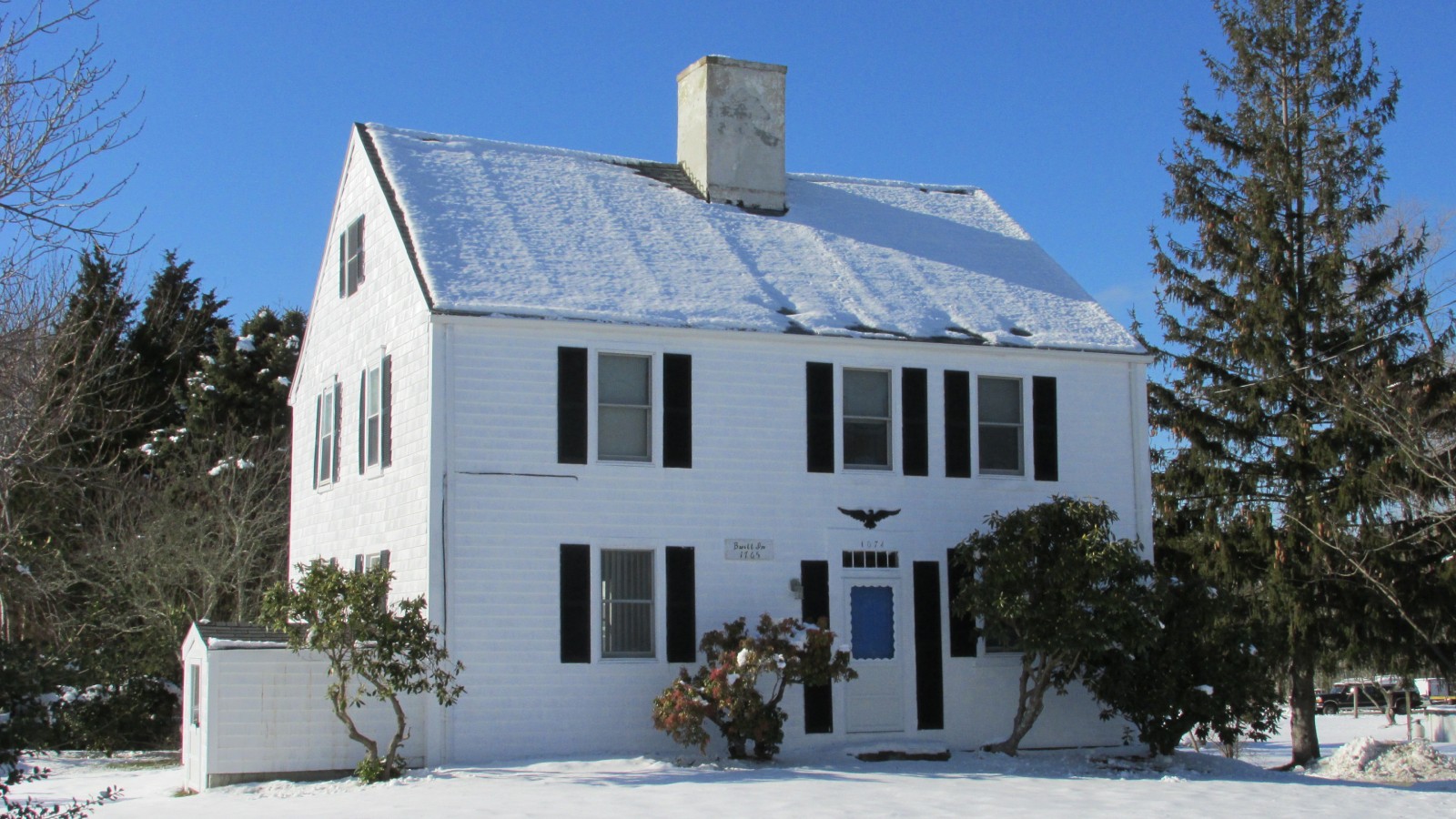 A white center-chimney house with black shutters in winter snow