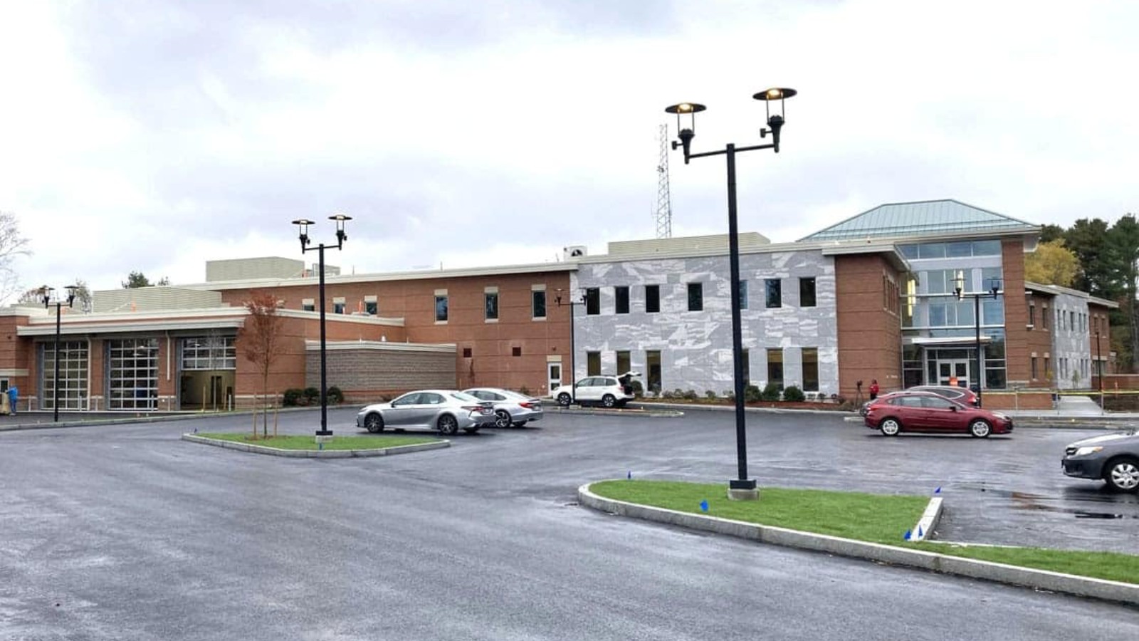 Taunton's new Public Safety Facility at 90 County St., a two-story brick and gray stone building with garage bays at left and a glass entrance at right, seen across a newly paved parking lot under a cloudy sky