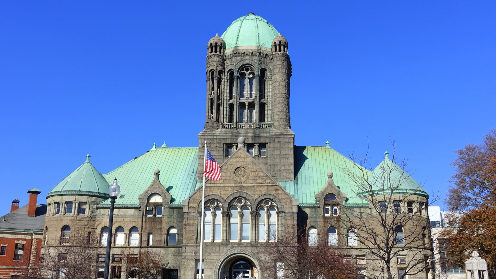 The Bristol County Superior Court in Taunton, a granite courthouse with a green copper dome on its central tower, copper roofs and round corner turrets, with an American flag flying in front