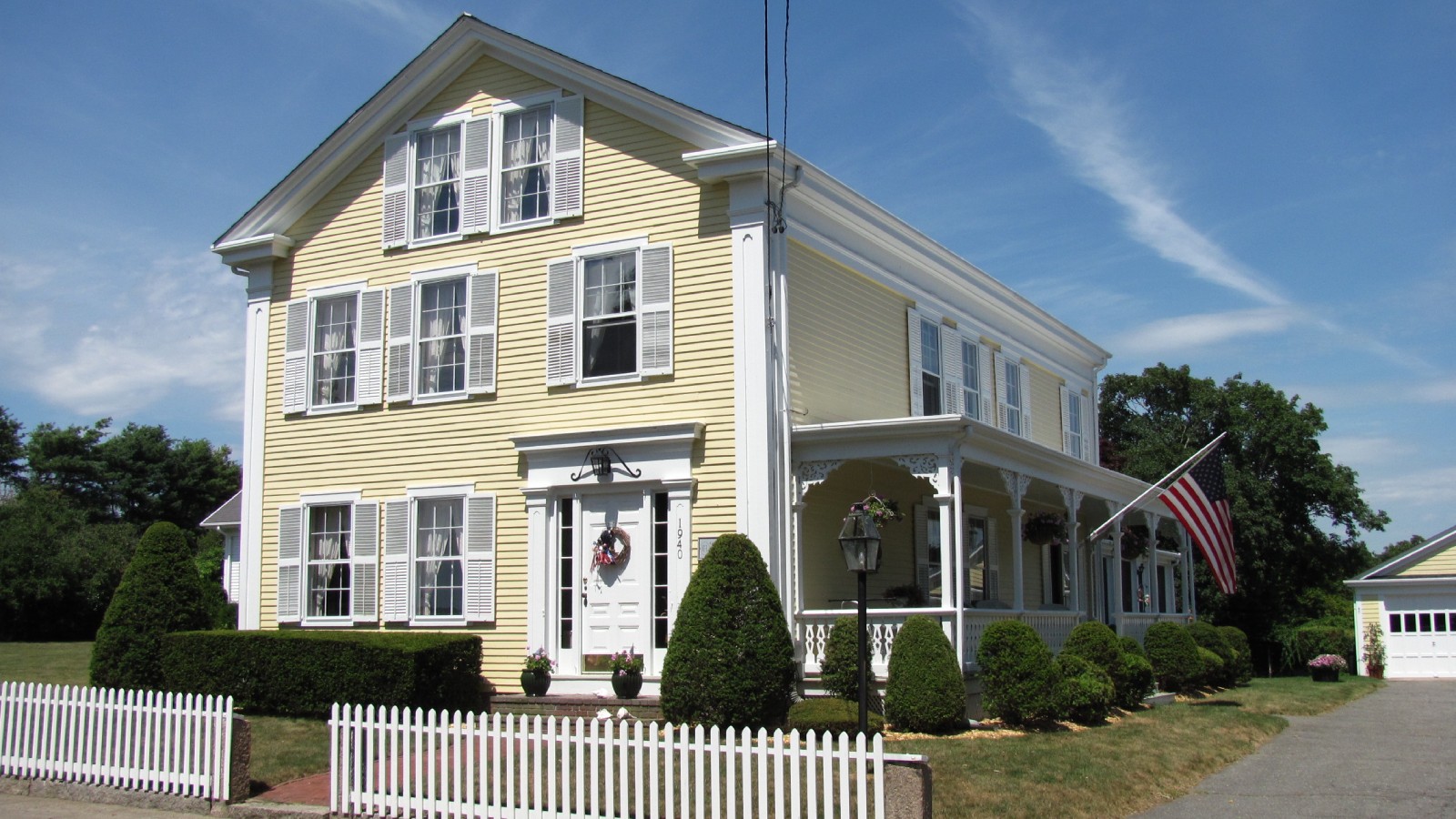 A pale yellow house with black shutters behind a white picket fence at Westport Point