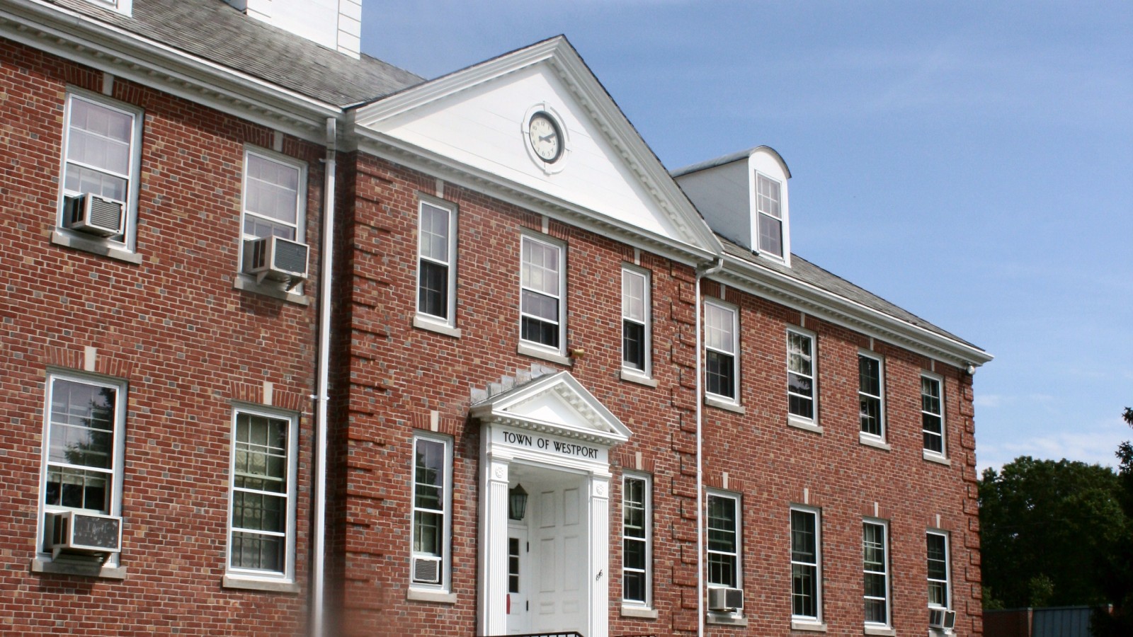 Westport Town Hall, a red brick building with a white pediment and clock, and TOWN OF WESTPORT over the front door, under a blue sky